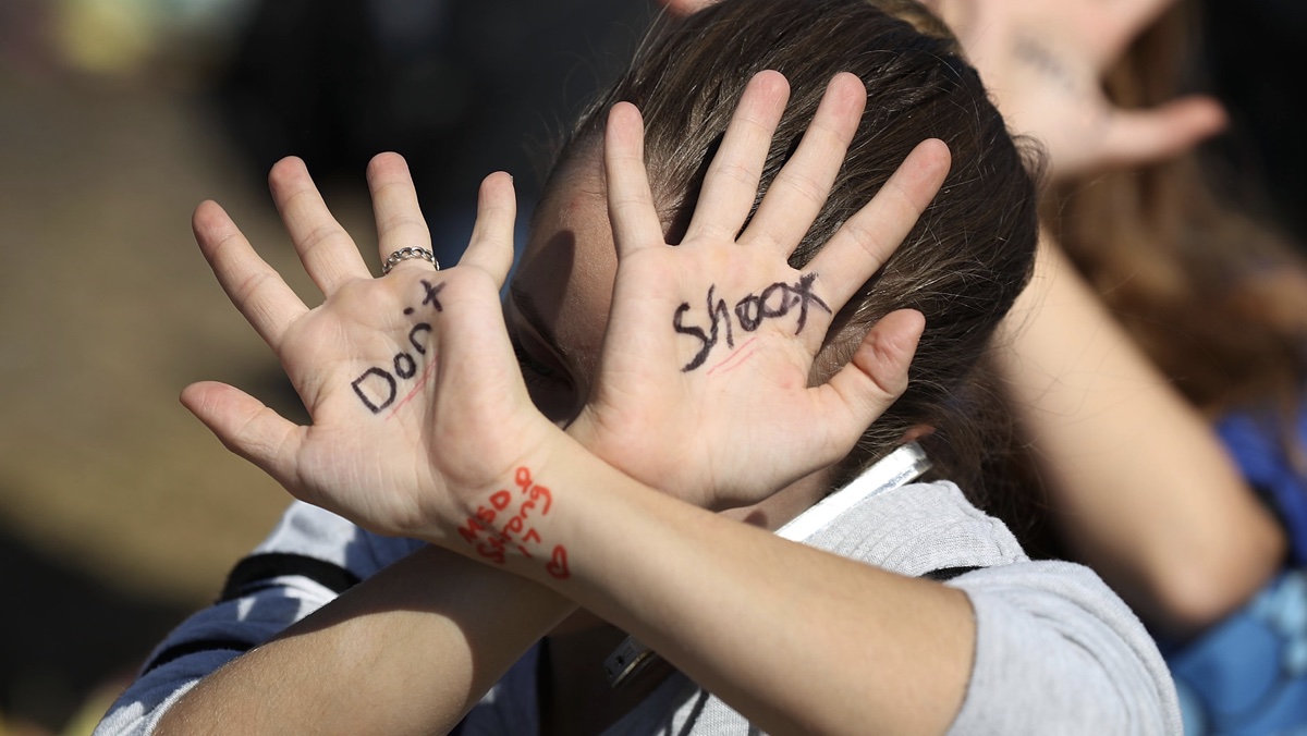 Child holds up two palm with the word "don't" written on one and "shoot" on the other.